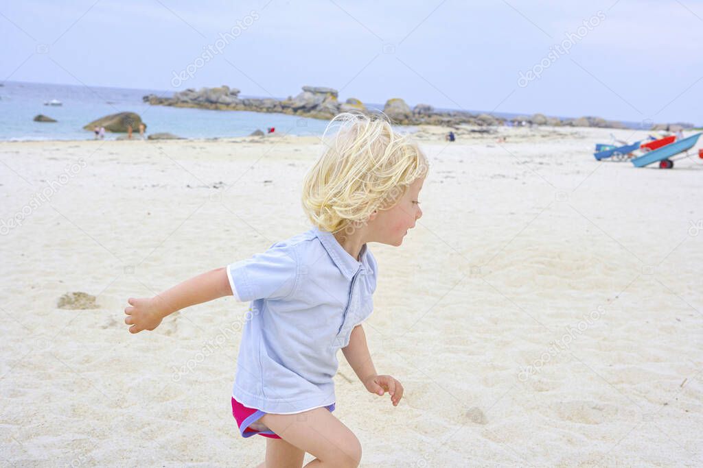 Happy cute active little boy playing in the sand at a beach in Brittany