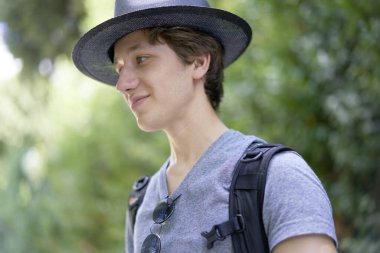 Yaz tatilinde güzel yeşilliklerde mutlu bir şekilde gülümseyen şapkalı genç bir adam.