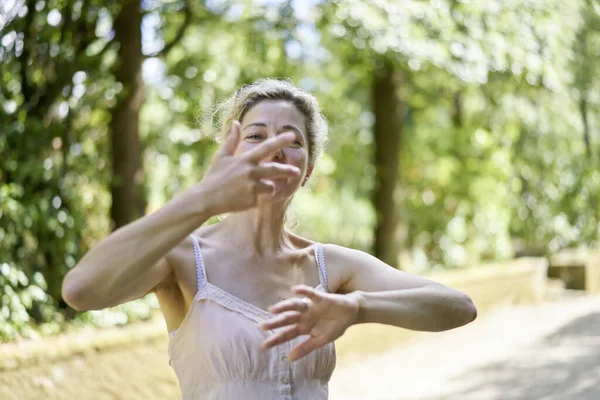 Woman doing relaxation moves like tai chi chi gong exercises in the greenery of a summer park