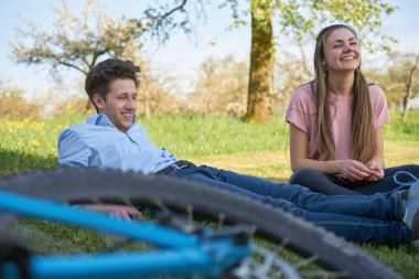 Güler yüzlü arkadaşlar, güneşli bir günde ağaçlarla çayırlarda bisiklet sürerek vakit geçirirler.