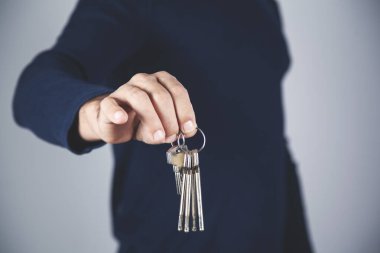 Gri arka planda anahtarı tutan genç adam.