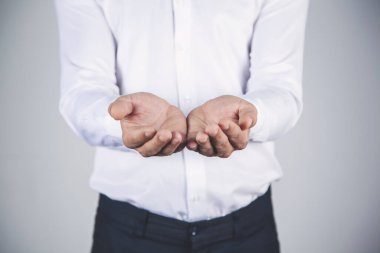 İş adamı gri duvar arkaplanına avuçlarını boşaltır