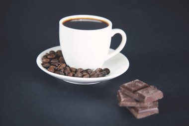 Koyu arkaplanda tahıllar olan bir fincan kahve.