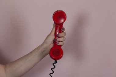 Pembe arka planda kırmızı telefon tutan kadın.