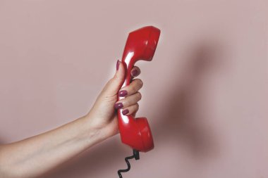 Pembe arka planda kırmızı telefon tutan kadın.