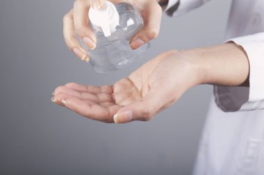 Kadın, gri arka planda mikrop önleyici sıvı jel kullanıyor.