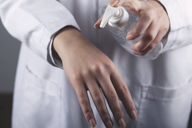 Kadın, gri arka planda mikrop önleyici sıvı jel kullanıyor.