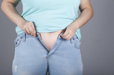 Kadın gri arka planda dar pantolon giyiyor.