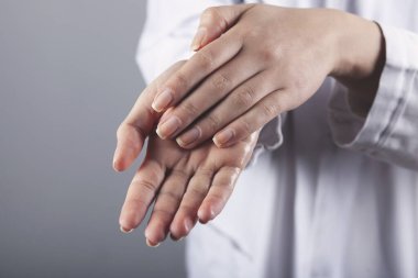 Doktor ellerini gri arka planda jel ile yıkıyor.
