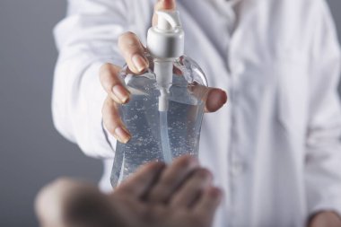 Kadın, gri arka planda mikrop önleyici sıvı jel kullanıyor.
