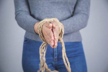 Gri duvar arkasında eli bağlı bir kadın.