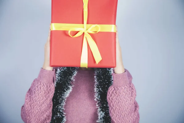 woman hand gift box on face on gray background