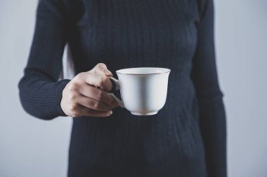 Gri arkaplanda bir fincan kahve ya da çay tutan kadın.