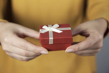 Gri arka planda hediye kutusunu tutan kadın.