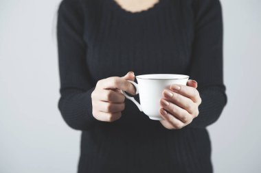 Gri arkaplanda bir fincan kahve tutan kadın.