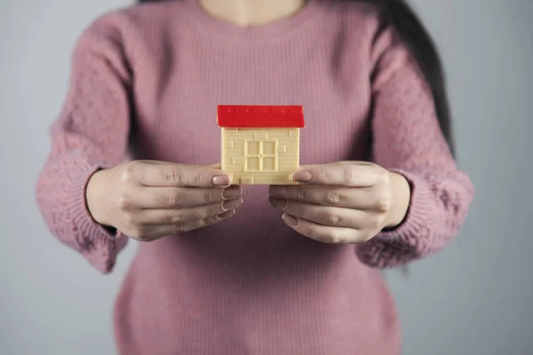 woman hand house model on gray wall background