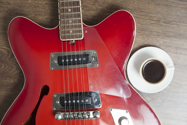 red guitar with cup of coffee on wooden background