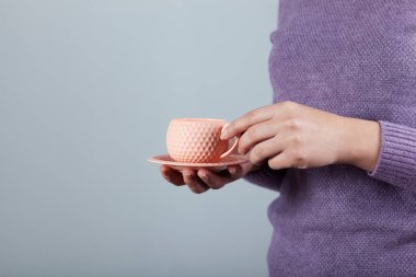 Bir fincan çay ya da kahve tutan bir kadın.