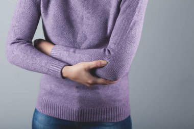 Gri arka planda dirseği ağrıyan kadın