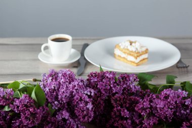 Tabakta kek ve masada leylak olan bir fincan kahve.