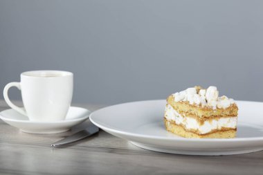 Tabakta kek ve masada leylak olan bir fincan kahve.