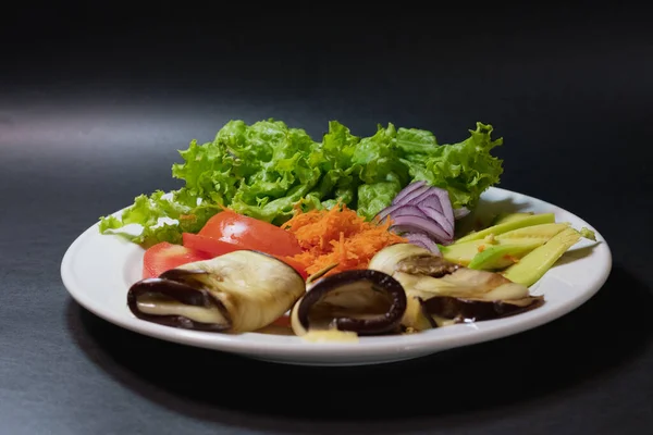 Sağlıklı vejetaryen yiyecekler, beyaz tabakta ve siyah arka planda, tabağın patateslerden, havuçlardan, domateslerden, marullardan ve avokadodan oluştuğunu görebiliyoruz.