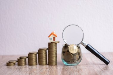 Bozuk para üzerinde küçük bir ev. Merdivenden merdivene kadar uzanır. Cam şişedeki bozuk para büyüteçle kaplanmış. İpotek konsepti, ev inşaatı, kiralama, ev bulma