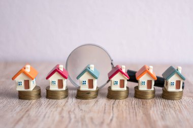 Büyüteçle bozuk para yığınının üzerinde minyatür bir model ev. Konut kredisi inşaatı. Yatırım analizi. Gelecekteki ailelere ev aramak da dahil..