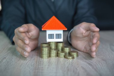 Turuncu çatı katı. Bir yığın bozuk para koy. Ev sigortası konsepti. Bir işadamı turuncu bir evi korur. Bir satış temsilcisinin evini mesaj alanı ile korur..