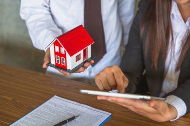 Bir iş adamının elinde kırmızı bir ev. Yatırımcılar onları dizüstü bilgisayarlardan, konseptlerden, evlerden, kiralık gayrimenkul konutlarından ev kredilerine kadar analiz etmeyi düşünüyorlar..