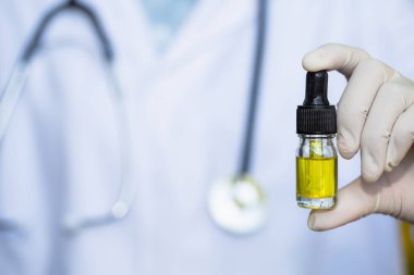 Cam şişe sapı, CBD kenevir yağı. Doktorlar ya da araştırmacılar bir şişe kenevir yağı tutuyor. Tıbbi steteskopla geçmiş. Tıbbi marihuana konsepti, CBD kenevir yağı. kenevir ürünü, kapat