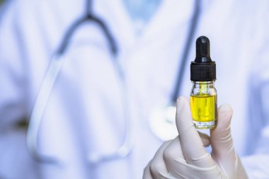 İçinde CBD kenevir yağı bulunan cam şişe bir araştırmacının ya da tıbbi ekibin elinde. Tıbbi steteskopla arka plan. Kenevir yağı, kenevir ürünleri Hastalıkların tedavisi için tıbbi marihuana