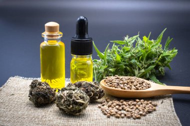 Cam şişedeki kenevir yağı. Ahşap bir kaşıkta kenevir tohumu ve kenevir yaprakları masaya konur. Marihuana yapraklarının doğal hastalıklar için yağ olarak çıkarılması fikri. Doğal bitkisel ilaçlar..