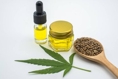 Cam şişedeki kenevir yağı. Ahşap bir kaşıkta kenevir tohumu ve kenevir yaprakları masaya konur. Marihuana yapraklarının doğal hastalıklar için yağ olarak çıkarılması fikri. Doğal bitkisel ilaçlar..