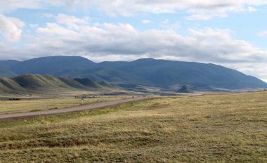 Beyaz bulutlar Sayan Dağları Sibirya Rusya ile mavi gökyüzü altında sarı çim ile geniş bozkır