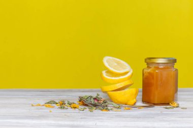 Limon dilimleri havada süzülüyor. Bal ve sarı arka planda çay otları olan bir masada.