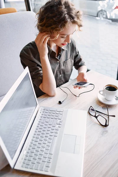 Kvinne med laptop og telefonavlyttingsmusikk på kafe – stockfoto