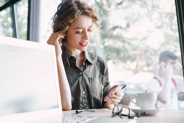Nainen kannettava tietokone ja puhelin kuuntelee musiikkia kahvilassa — kuvapankkivalokuva