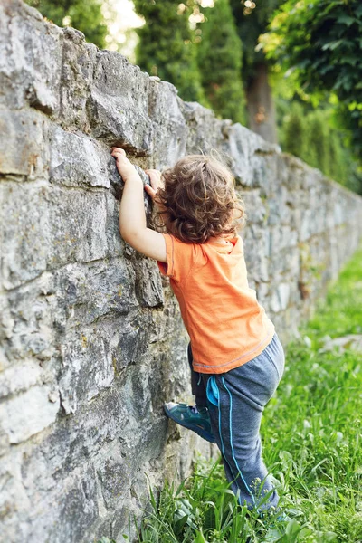 A little boy tries to climb a stone wall — Stock Photo, Image