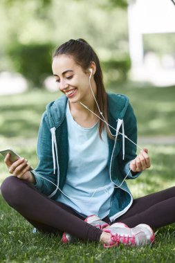 Spor giyim ile smartphone Park çimlerde oturan genç ve sportif kadın portresi