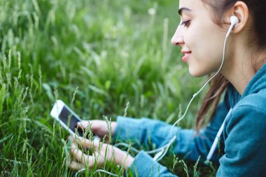 Spor giyim genç ve sportif kadın portresi ile smartphone Park çimenlerin üzerinde yatıyor