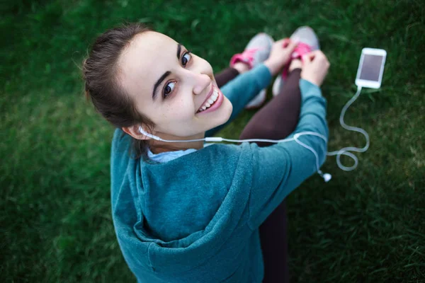 Portrait of young and sporty woman in sportswear Lies with the smartphone on the grass in park — Stock Photo, Image