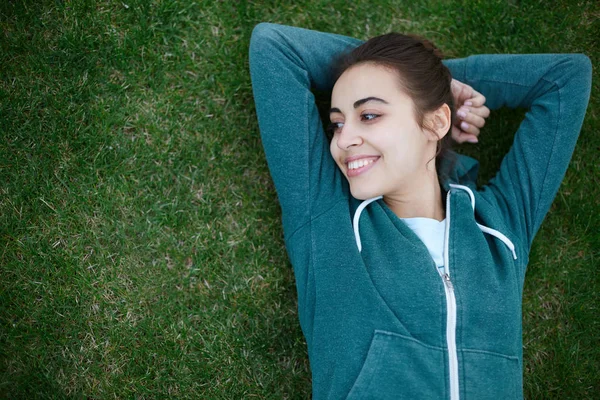 Portrait of young and sporty woman in sportswear lies on the grass in park — Stock Photo, Image