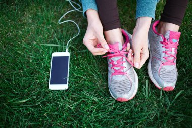 park ve bağları çim üzerinde spor ayakkabı bağcıkları kadar smartphone ile spor giyim sportif kadın oturur
