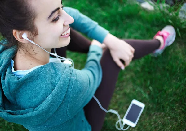 Portrait of young and sporty woman in sportswear Lies with the smartphone on the grass in park — Stock Photo, Image