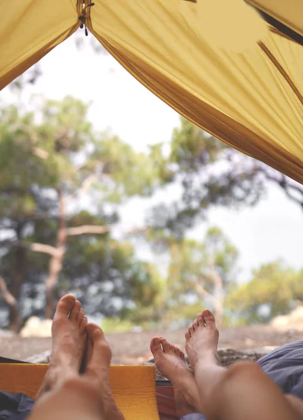 Utsikt fra innsiden av et telt i skogen og beina til to personer kommer ut av teltet – stockfoto