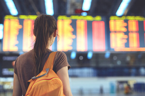 Young woman in international airport looking at the flight information board