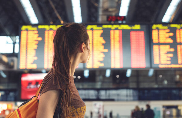 Young woman in international airport looking at the flight information board