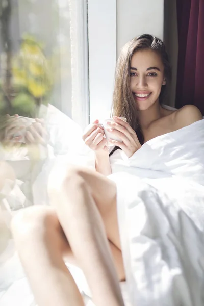 Eine Frau sitzt mit einer Tasse Kaffee auf der Fensterbank — Stockfoto