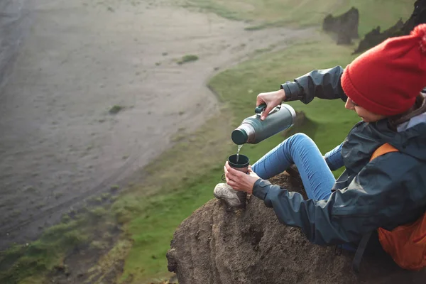 Nainen patikoija reppu istuu vuoren huipulla ja nauttia auringonlaskusta Islannissa — kuvapankkivalokuva